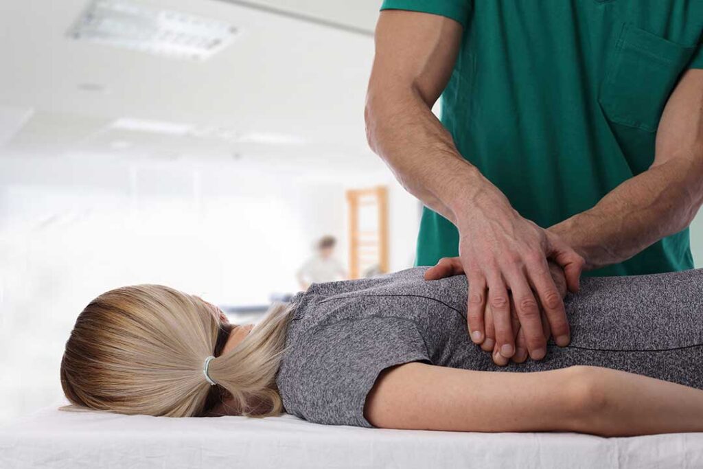 Clinician assessing a seated adult with shoulder and back pain using gentle movement tests.